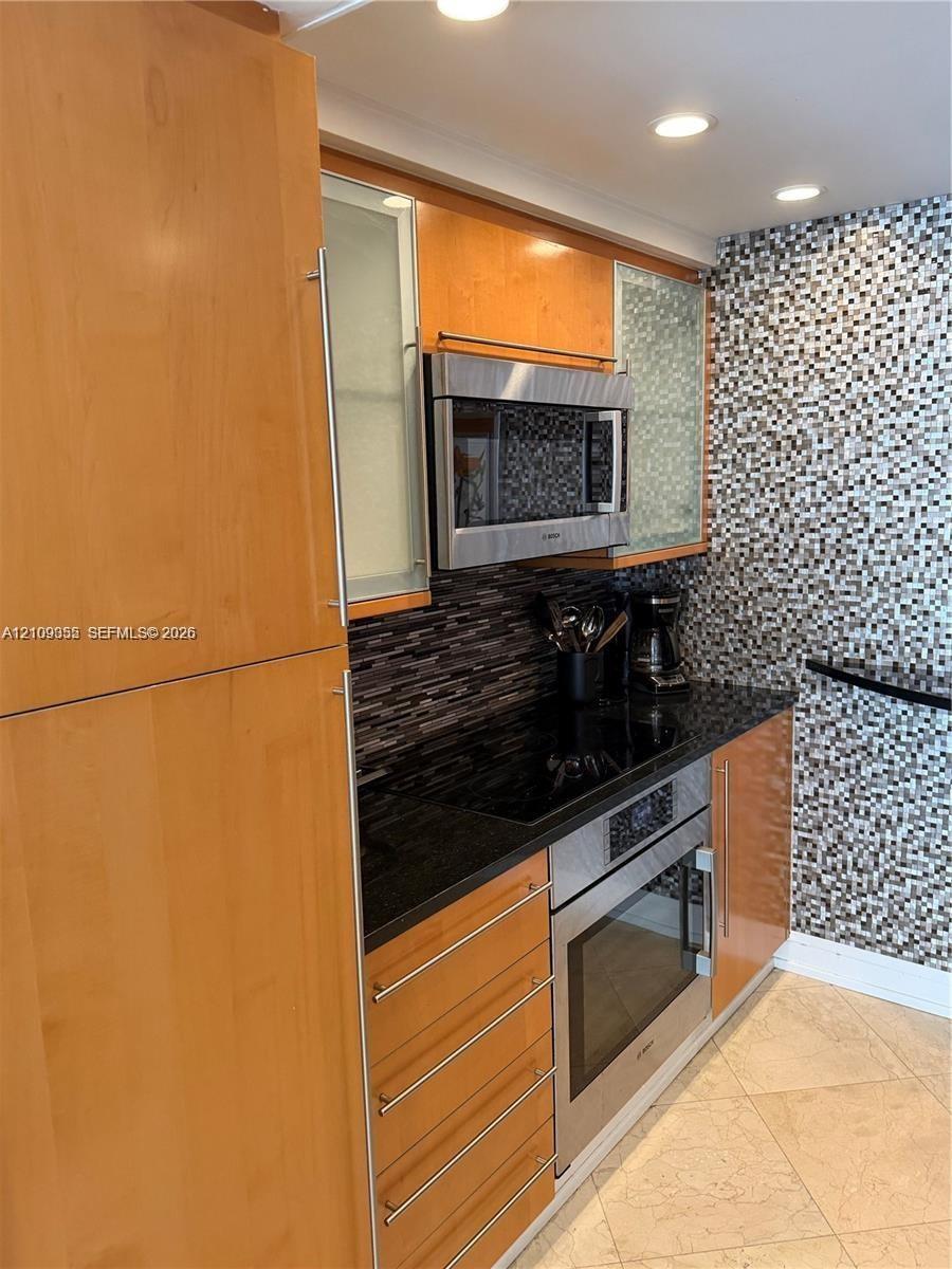 Flat-panel wood cabinetry with frosted glass inserts, stainless steel built-in microwave, integrated electric cooktop, stainless steel oven, and mosai