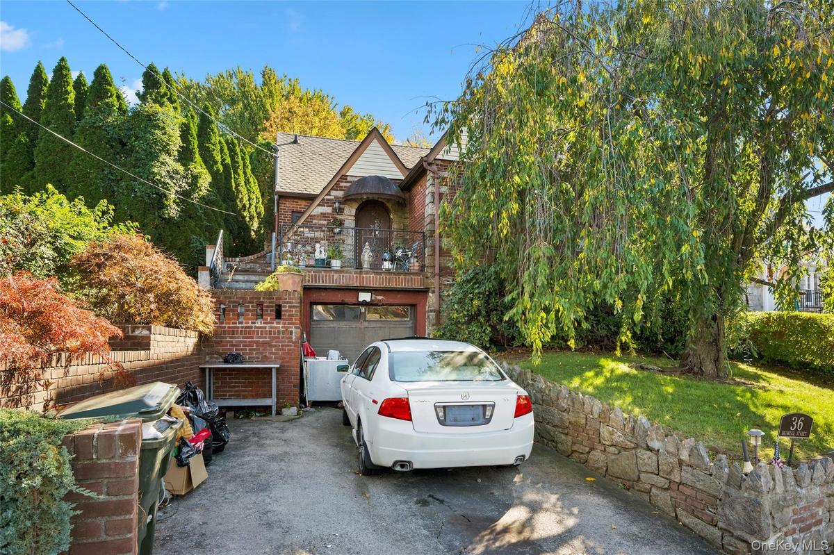 Brick exterior with stone accents, arched entryway, balcony with metal railing, attached garage, and stone retaining wall