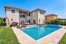 Two-story stucco exterior with a tile roof, featuring a private swimming pool, integrated spa, and natural stone patio decking
