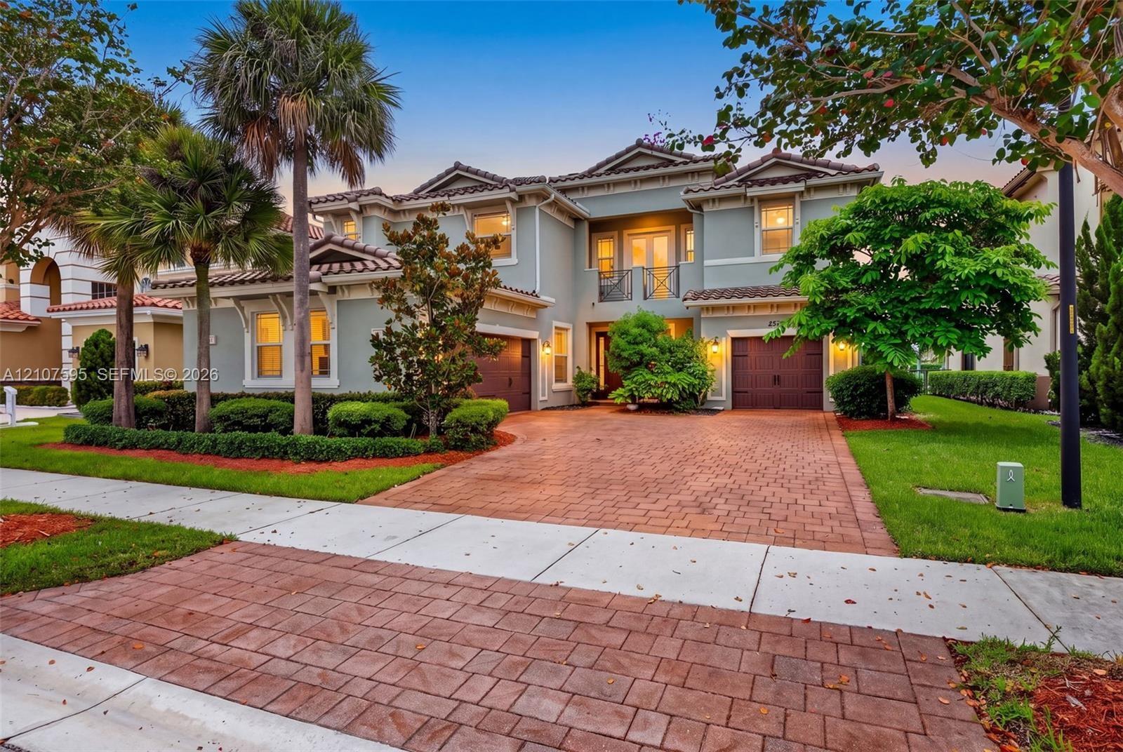 Two-story residence featuring a tile roof, stucco exterior, paver driveway, attached two-car garage, and second-story balcony with decorative metal ra