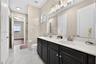 Double vanity with dark cabinetry, stone-finish countertops, dual under-mount sinks, and large wall-mounted mirror, featuring porcelain tile flooring 