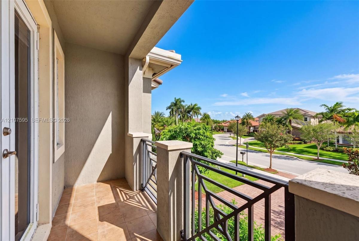 Covered balcony featuring tile flooring, stucco columns, and a decorative metal railing