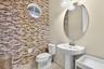 Stacked stone accent wall, oval wall-mounted mirror, white pedestal sink with polished nickel faucet, and circular window