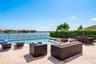 Stone-paved patio featuring a swimming pool, integrated spa, metal perimeter fencing, and mature hedge landscaping