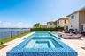 In-ground swimming pool and spa featuring blue tile accents, surrounded by a light-toned stone paver deck and metal perimeter fencing