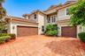 Stucco exterior featuring a tile roof, brick-style paver driveway, two-car garage, and upper-level balcony with metal railing