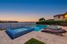 In-ground swimming pool and raised spa with blue tile accents, surrounded by a stone-paver deck, enclosed by a perimeter fence, overlooking a water fe