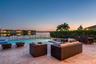 Rear patio featuring travertine pavers, a rectangular swimming pool, a spillover spa, and a metal perimeter fence overlooking the water