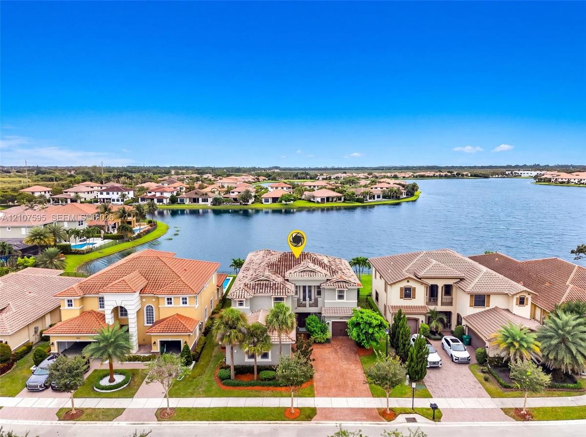 Waterfront property featuring a multi-story exterior with a tile roof, paved driveway, and mature landscaping