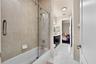 Bathroom featuring a tub-shower combination with floor-to-ceiling neutral tile surround and glass sliding doors, dark wood-finish cabinetry, stone-sty