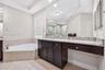 Built-in dark wood vanity featuring a speckled stone countertop, large-scale wall-mounted mirror, corner jetted soaking tub with tile surround, and ne