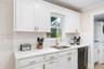 Kitchen featuring white cabinetry, light-toned stone-finish countertops, brass-toned hardware, subway tile backsplash, and an undermount sink with a m