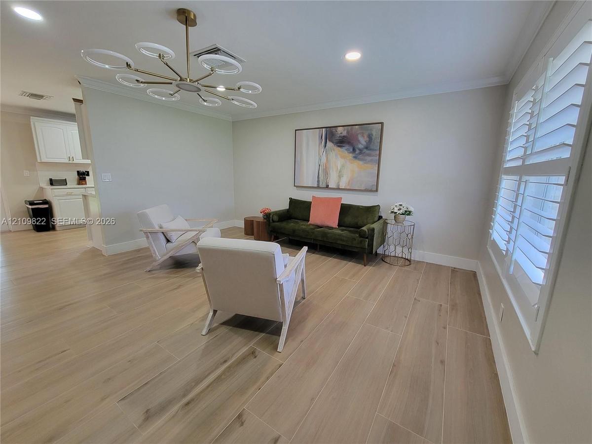 Wood-finish flooring, contemporary multi-ring chandelier, recessed lighting, and white plantation shutters