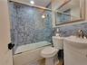Full bathroom featuring a tub-shower combination with glass sliding doors, honeycomb-patterned tile surround, vanity with an integrated basin, brushed