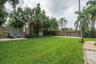 Expansive backyard featuring a lush lawn, mature palm trees, perimeter wood fencing, stone paver accents, and decorative pebble ground cover