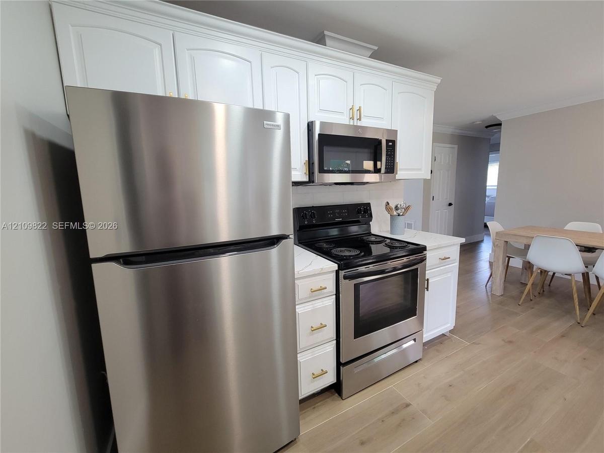 Kitchen featuring white shaker-style cabinetry with gold-toned hardware, stainless steel appliances, stone-finish countertops, and wood-finish floorin
