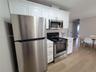 Kitchen featuring white shaker-style cabinetry with gold-toned hardware, stainless steel appliances, stone-finish countertops, and wood-finish floorin