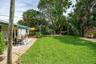 Backyard featuring a paved stone patio, mature canopy trees, lush lawn, and palm-lined perimeter
