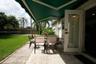 Paved stone patio featuring a retractable green awning, glass-paneled entry door, fenced perimeter, and mature palm landscaping