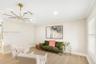 Spacious room featuring wood-finish tile flooring, crown molding, tiered gold-tone chandelier with integrated circular lighting, and plantation shutte