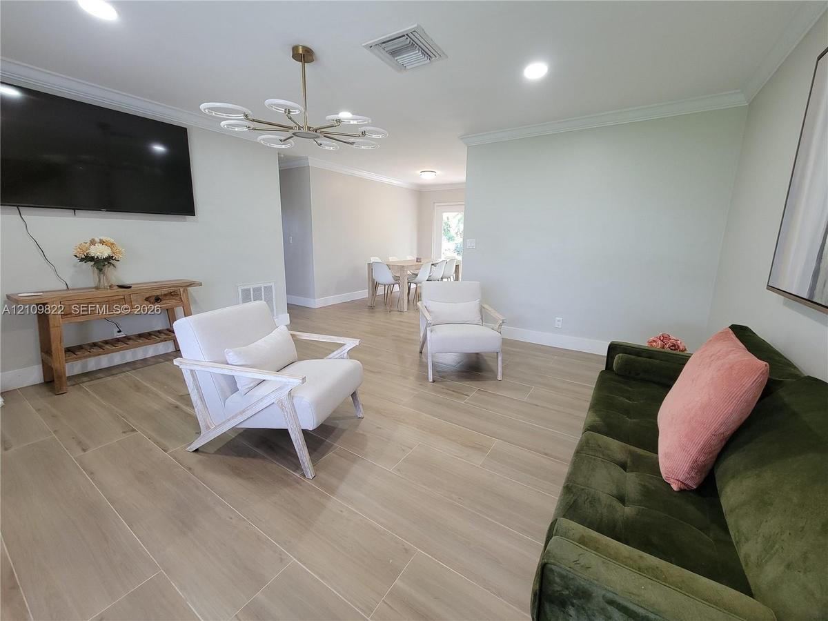 Open-concept living space featuring wood-finish tile flooring, crown molding, recessed lighting, and a multi-arm modern light fixture