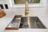 Undermount stainless steel kitchen sink featuring a brass high-arc pull-down faucet, stone-finish countertops, and subway-tile backsplash