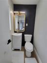 White pedestal sink with a metallic faucet, black hexagonal tile accent wall, gold-finish framed mirror, and wood-finish flooring