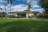 Expansive backyard featuring a manicured lawn, paved patio, retractable awning, mature palms, and metal raised garden beds