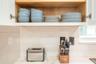Upper cabinetry featuring natural wood-tone interior shelving, stone-composite countertop, and a horizontal-set rectangular tile backsplash