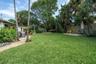 Backyard featuring a manicured lawn, flagstone pathway, mature shade trees, palm landscaping, and a gravel hardscape area