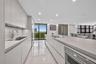 Kitchen featuring flat-panel cabinetry, a quartz waterfall-edge island with an integrated cooktop, stone-finish flooring, a stainless steel wine refri