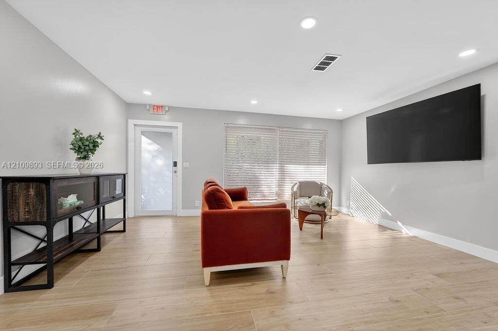 Spacious interior featuring neutral wall tones, recessed lighting, wood-finish tile flooring, and a glass-paneled exterior door