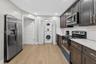 Kitchen featuring dark-stained shaker cabinetry, stainless steel appliances, light-toned stone-finish countertops, wood-finish flooring, and an integr