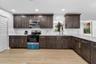Kitchen featuring dark-finish cabinetry with brass-tone hardware, stone countertops, white subway tile backsplash, stainless steel appliances, and woo
