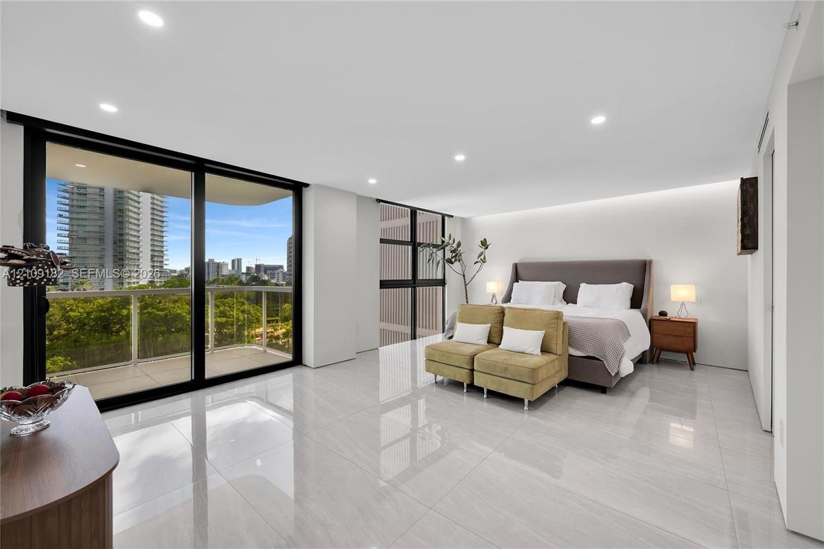 Light-filled Primary Bedroom featuring large-format polished tile flooring, floor-to-ceiling glass sliding doors, and a private balcony with a metal r