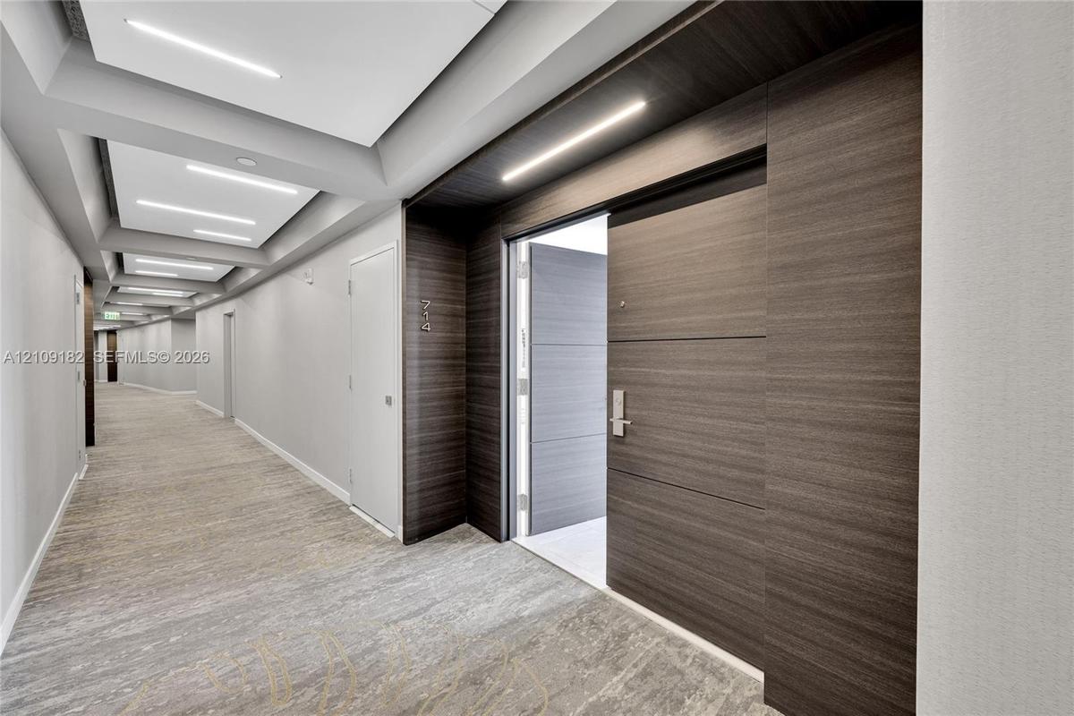 Hallway featuring recessed tray ceiling lighting, wood-finish wall paneling, and neutral carpeting