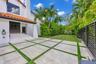 Exterior facade featuring white stucco walls, clay tile roofing, concrete paver patio with turf ribbon accents, and horizontal slat perimeter fencing