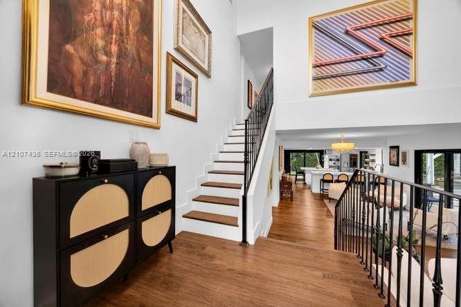 Foyer featuring a high ceiling, wood-finish flooring, and a staircase with wood treads and a black metal railing