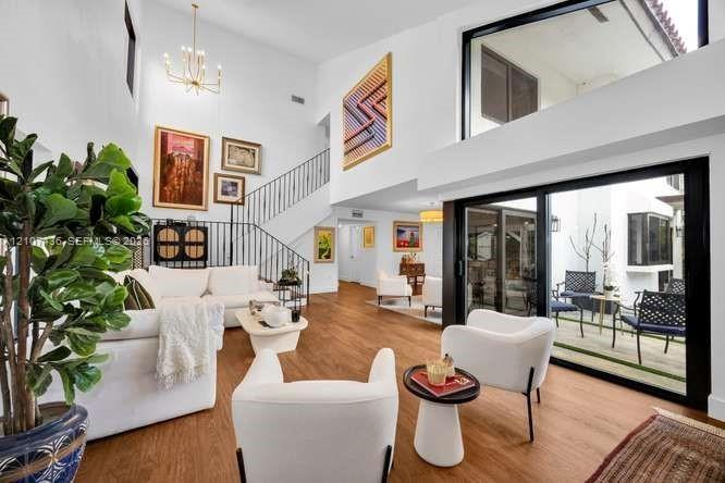 Double-height living area featuring wood-finish flooring, a tiered chandelier, black metal staircase railings, and floor-to-ceiling sliding glass door