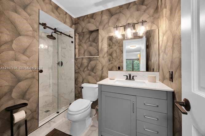 Bathroom featuring a gray vanity with a white countertop, glass-enclosed shower with sliding hardware, patterned wall covering, built-in shower niche,