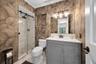 Bathroom featuring a gray vanity with a white countertop, glass-enclosed shower with sliding hardware, patterned wall covering, built-in shower niche,