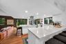 Modern kitchen featuring an expansive central island with quartz countertops, custom white cabinetry, stainless steel range hood, recessed lighting, a