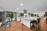 Kitchen featuring a large central island with light-toned solid surface countertops, white cabinetry, stainless steel range hood, built-in wall oven, 