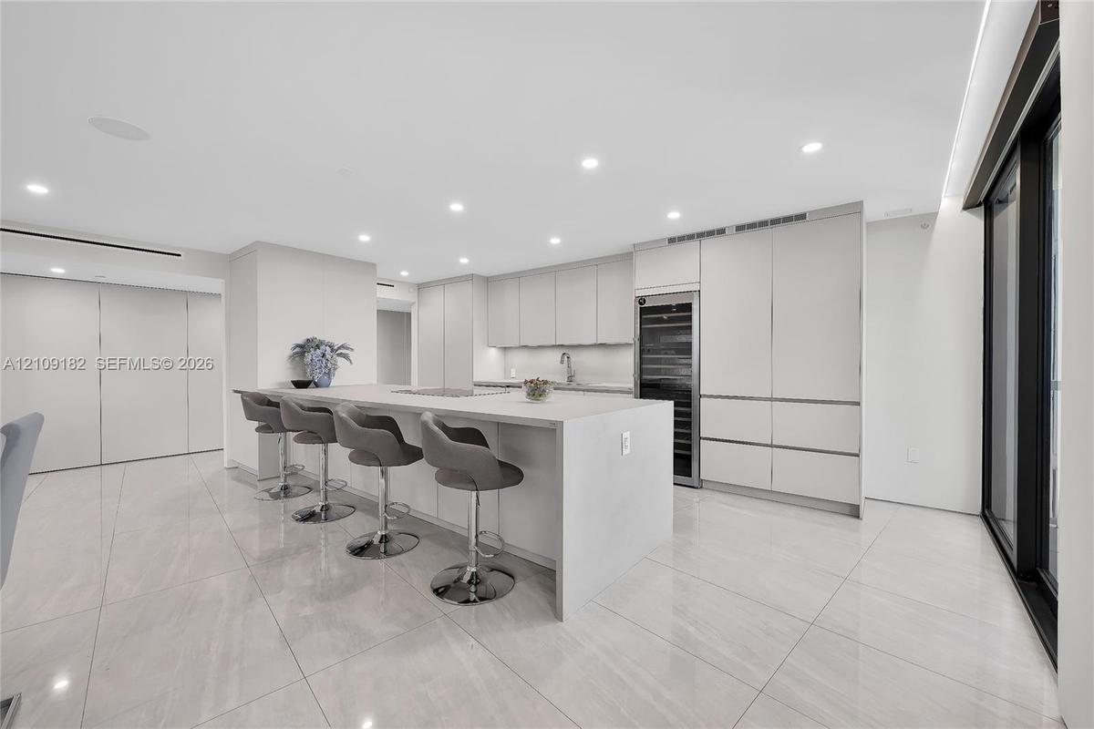 Open kitchen featuring flat-panel cabinetry, a central island with a solid-surface countertop, built-in wine refrigeration, and polished stone-finish 