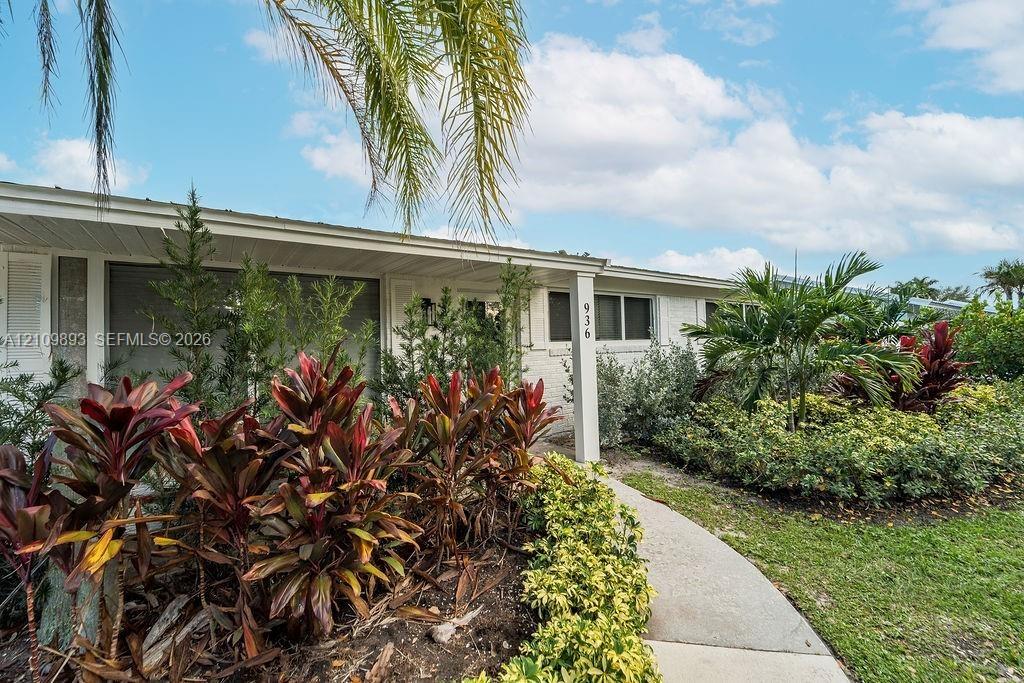 White-painted brick exterior featuring a covered front entryway, concrete walkway, and lush tropical landscaping