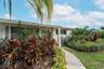 White-painted brick exterior featuring a covered front entryway, concrete walkway, and lush tropical landscaping