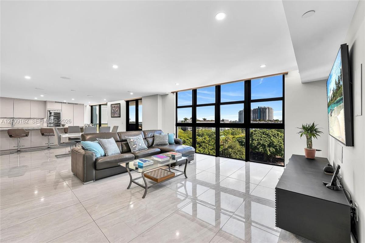 Open-concept living space featuring floor-to-ceiling windows with black mullions, large-format polished tile flooring, recessed lighting, and built-in