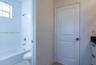 Bathroom featuring a composite bathtub with wall-mounted shower hardware, high-profile window, white shaker-style cabinetry with dark countertop, and 