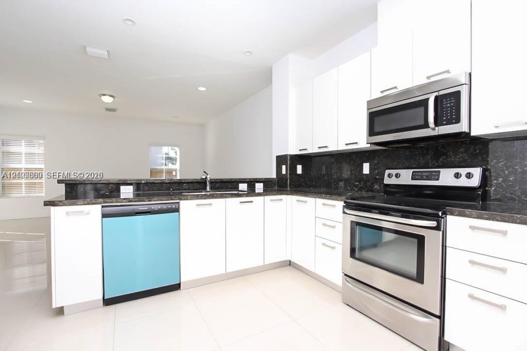 Kitchen featuring white cabinetry, dark stone countertops, stainless steel appliances, and large-format tile flooring