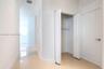 Hallway featuring polished tile flooring, white bi-fold closet doors, a solid-core panel door with a brushed nickel lever handle, and smooth-finish wa
